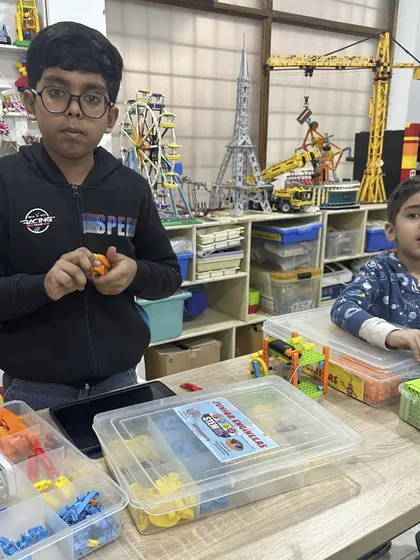 Two boys are deeply engaged in their LEGO projects at a table filled with building kits. The classroom setting, with large models in the background, shows the immersive world of engineering we create.