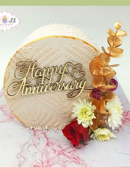 A beautiful anniversary cake with an intricate piped pattern, topped with fresh flowers and a wooden topper.