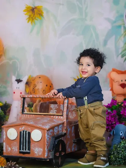 A happy toddler stands by his jeep in our lush jungle setup, complete with animal-print balloons and lots of greenery.
