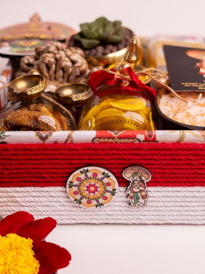 A close-up of the 'Ponnonam' hamper, focusing on the exterior details. The box is wrapped in red and white thread and adorned with custom-designed Mahabali and pookkalam-themed pins, adding a unique, personal touch.