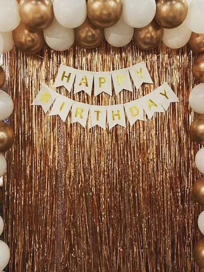 A classic birthday backdrop with a gold fringe curtain. A 'Happy Birthday' banner is framed by a simple yet elegant white and gold balloon arch.