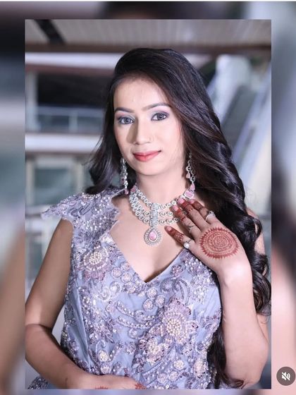 A smiling portrait of the model in the lavender-grey gown, holding her hand up to show the matching ring and henna design.