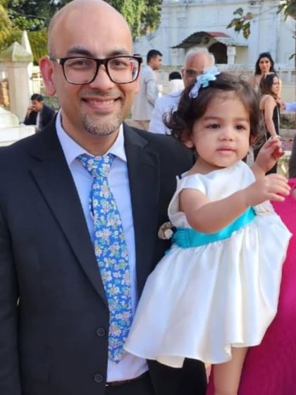 A proud father with his little girl, who is dressed in a simple yet elegant white satin dress with a bright blue sash. It's a perfect example of how a pop of color can personalize a classic look.