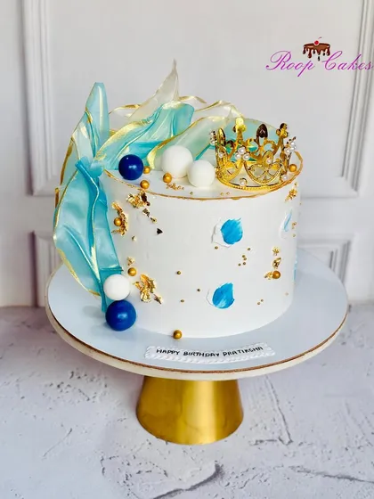 Royalty in every bite. This stunning cake features abstract blue sails, a golden crown, and artistic paint strokes for a modern and regal look.