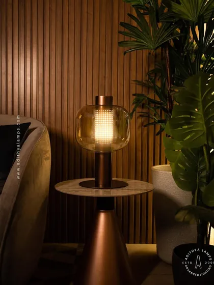 This elegant table lamp features a perforated inner core within a glass shade, creating a mesmerizing light pattern. Placed on a side table, it provides warm, decorative light that enhances the cozy atmosphere of a living room.