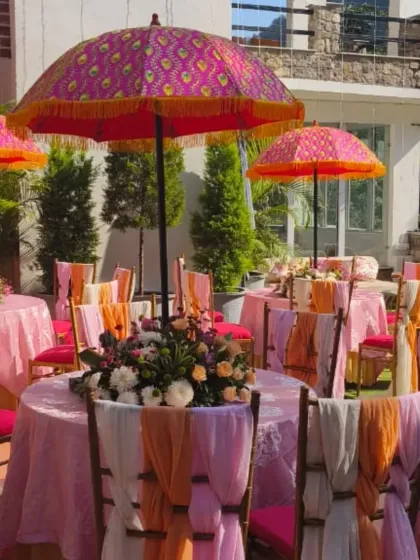 A colorful Mehendi setup for a destination wedding in Rishikesh. We used vibrant Rajasthani-style umbrellas, bright pink and orange chair drapes, and fresh floral centerpieces to create a festive atmosphere.