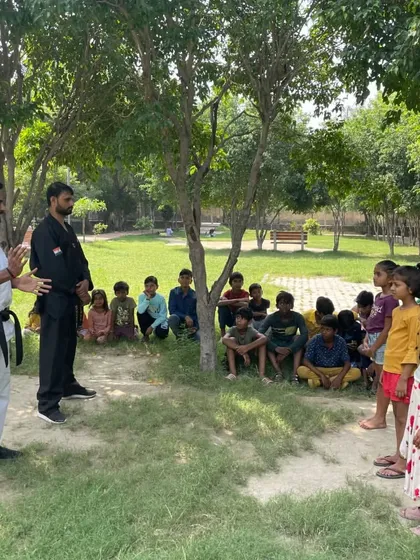 I regularly conduct self-defense workshops and martial arts classes for kids in outdoor settings like parks and society grounds. Here, I am explaining a technique to a group of young learners.