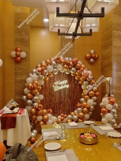 A sophisticated restaurant table setup for a birthday, with a rose gold and silver balloon ring backdrop.