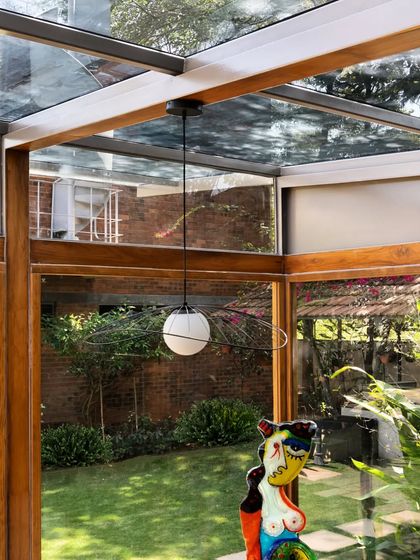 The reflection of the garden in the glass roof and walls creates a layered, immersive experience of being in nature.