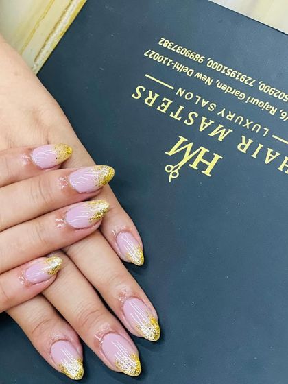 This view showcases our gold glitter fade nails against our salon's branded background. The almond shape elongates the fingers, while the glitter adds a festive touch that is both chic and celebratory.