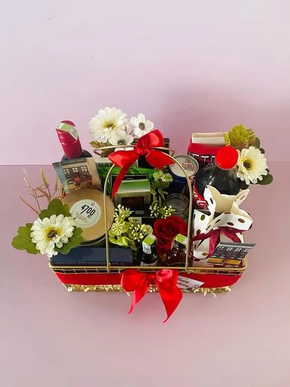 A celebration hamper in a metal basket. This one is curated with non-alcoholic wine, snacks, and a quirky cow-shaped creamer.