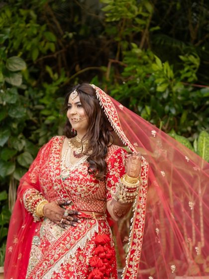 The bride playing with her veil. The red lehenga and soft makeup create a classic yet playful bridal look.