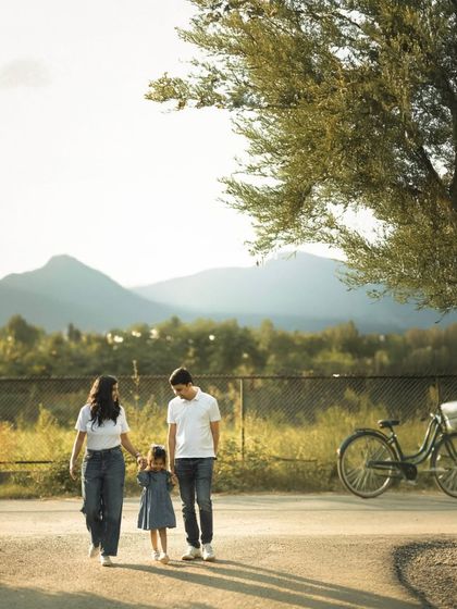 Holding hands, a family takes a leisurely walk down a path with mountains in the distance. The setting sun casts long shadows, capturing a simple, beautiful moment of togetherness during their outdoor family portrait session.