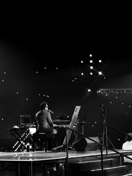 A solitary moment of A.R. Rahman on stage against a backdrop of thousands of phone lights. This image captures the profound connection between the artist and his audience that we strive to facilitate.