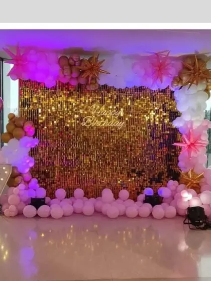 A glamorous 75th birthday party with a gold sequin wall. The decor features pink and white balloons, starburst props, and large light-up numbers.