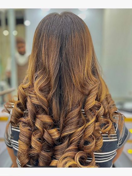 This client's hair features a beautiful balayage with golden and caramel tones, styled into tight, bouncy curls that showcase the stunning color blend.