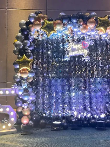 A glamorous photo booth for a 25th-anniversary party. The shimmering sequin backdrop, balloon arch, and large marquee numbers create the perfect spot for memorable photos.