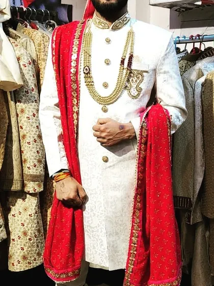A client trying on a classic white sherwani paired with a vibrant red embroidered stole. This combination is a popular choice for grooms, offering a look that is both traditional and striking.