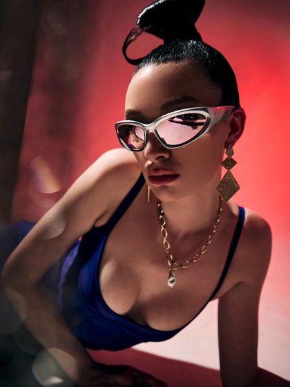 A close-up portrait emphasizing the futuristic sunglasses and gold chain necklace from the Mugler x H&M shoot. This shot highlights how accessories were used to build the high-fashion narrative.