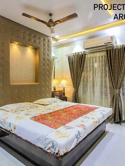 A bedroom in a Vashi duplex featuring a large, tufted headboard with an illuminated niche. The room is designed for comfort, with warm lighting and ample storage.