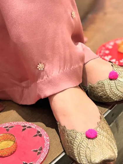Another look at the playful gold juttis with bright pink pom-poms, perfect for adding a touch of whimsy to your ensemble.