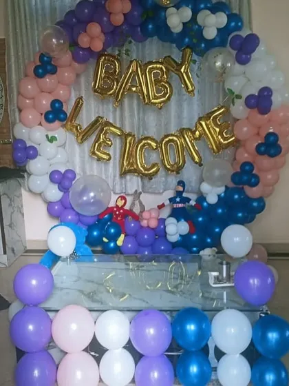 A 'Baby Welcome' party with a superhero twist. The balloon arrangement includes small cutouts of Iron Man and Captain America among the festive colors.