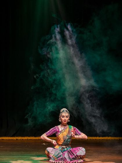 A seated pose from a performance, with dramatic smoke and lighting. This image captures the theatricality and visual artistry that can be part of a live dance show.