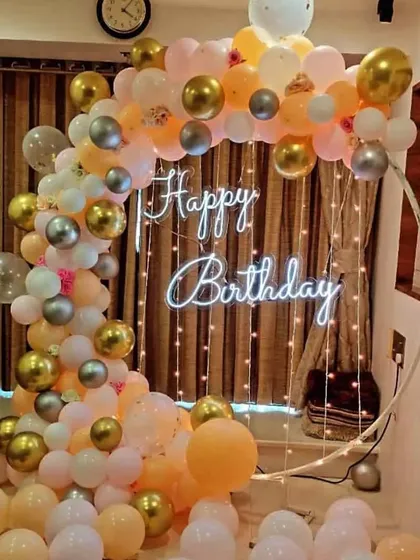 A peach, white, and gold balloon arch with a neon sign and fairy lights for a warm and celebratory home party.