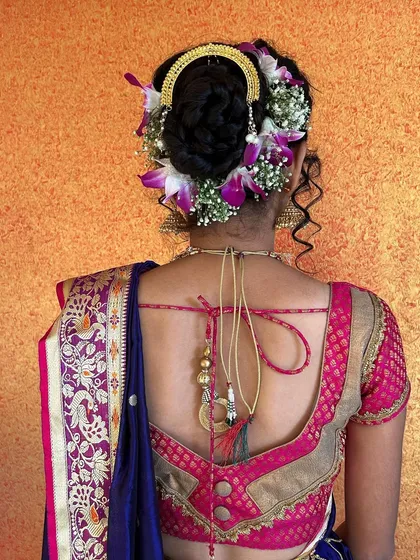A detailed look at the back of the bride, showcasing the elegant blouse design and the beautiful floral bun with a traditional 'ambada' accessory.