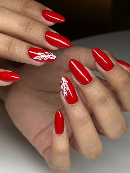 A classic red manicure with a touch of elegance. The simple, hand-painted white leaf design on the accent nails adds a delicate and artistic flair.