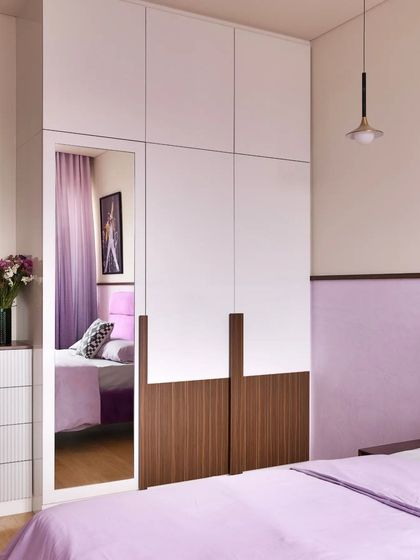 This full-height wardrobe combines white and wood-finish panels, with a built-in mirror that adds functionality and makes the room feel more spacious.