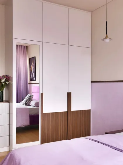 This full-height wardrobe combines white and wood-finish panels, with a built-in mirror that adds functionality and makes the room feel more spacious.