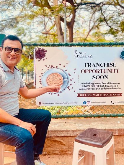 Our consultant points to a franchise opportunity banner for King's Coffee Co. in Mysore. This brand has grown from a small kiosk to a full-fledged cafe, and we are now helping them expand through franchising.