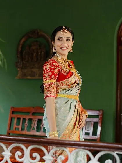 A bride on a balcony, her beautiful saree and jewelry pop against the rich green wall and traditional architecture.