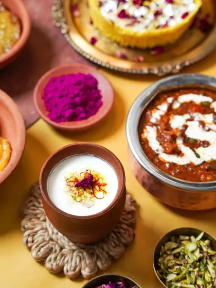 A festive corner of a Holi brunch table, featuring Dal Makhani and a glass of Lassi. The composition with colored powders and rustic coasters creates a warm and celebratory mood.