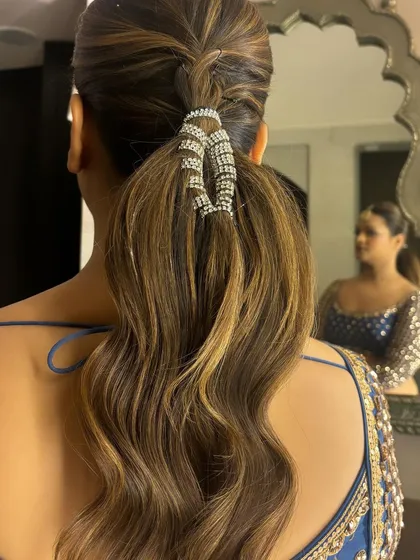 A close-up of the sparkling accessory on the braided ponytail, with the client's reflection in the mirror.