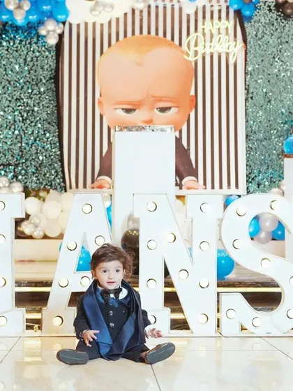 A solo shot of the birthday boy amidst his party's awesome decor. This photo highlights both the child and the fantastic "Boss Baby" themed setup with his name in lights.