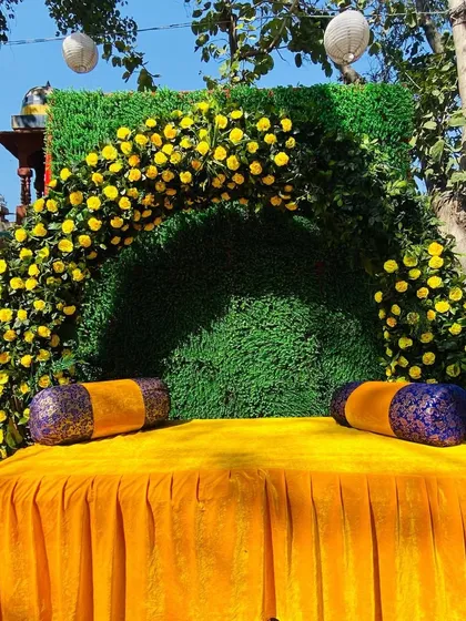 A simple and elegant Haldi seating idea, with a lush green backdrop accented by an arch of bright yellow flowers.