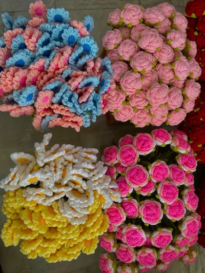 Piles of colorful crochet flower heads, including daisies and roses, waiting to be assembled into stems.