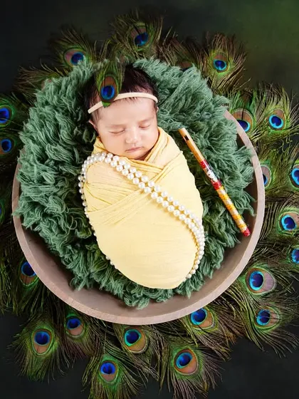 A creative and divine newborn photoshoot featuring a baby wrapped cozily as little Krishna, surrounded by a ring of peacock feathers. This is a special theme I offer to celebrate your faith and heritage.