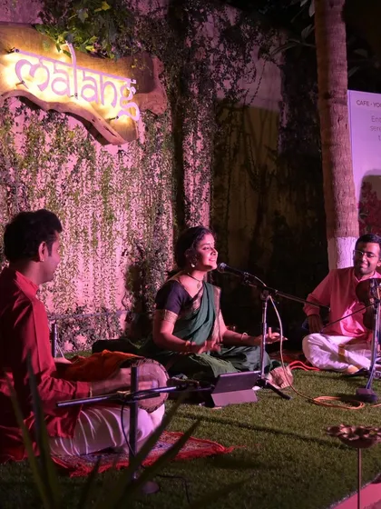 A different perspective of the Namma Ashram concert, showing the artists seated on the grass stage. This informal setup creates a very relaxed and engaging atmosphere.