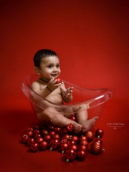 A playful moment during the red-themed bathtub shoot. The bright red background and shiny ornaments create a vibrant and energetic portrait that perfectly matches this baby's happy mood.