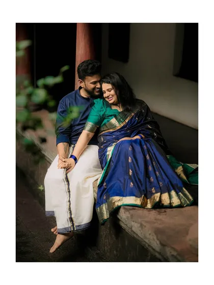 A tender moment shared on the veranda of a traditional Kerala home. The rich blue and green of their attire stand out against the rustic backdrop in this intimate pre-wedding portrait.
