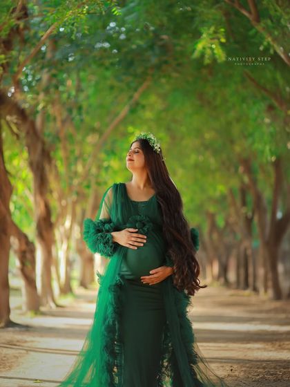 A serene outdoor portrait in a green gown. The mother-to-be is captured in a moment of quiet connection with her baby, surrounded by nature.