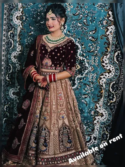 A beautiful dual-tone bridal lehenga with a maroon velvet blouse and a beige skirt featuring peacock motifs. This outfit is available for rent to make your wedding day perfect.