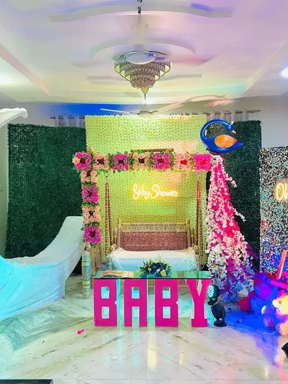 An elaborate baby shower stage in a home, featuring a moon prop, a decorated swing, a sequin wall, and a neon sign.