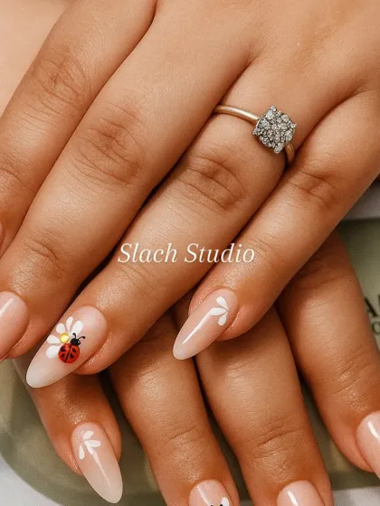 A touch of whimsy on these nude almond extensions. I hand-painted delicate white flowers and added a cute ladybug design on the ring finger for a unique and charming look.