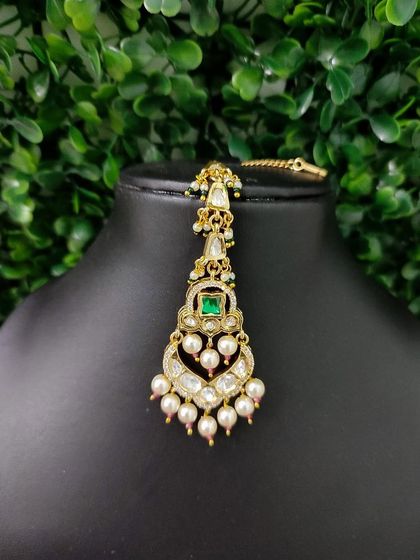 A simple yet elegant maang tikka with a square green stone and pearl drops.