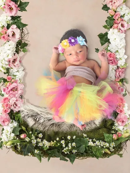 A newborn in a rainbow tutu, resting on a swing decorated with a cascade of fresh flowers.