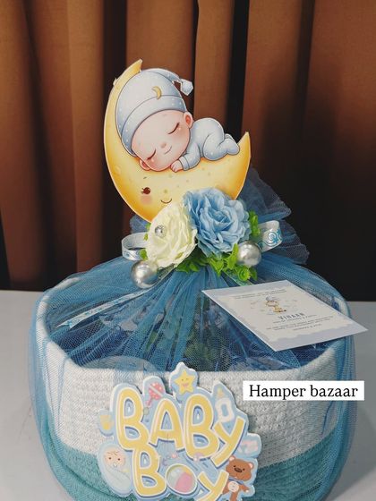 A close-up of the 'Baby Boy' hamper in a woven basket, topped with a cute cutout and delicate flowers.